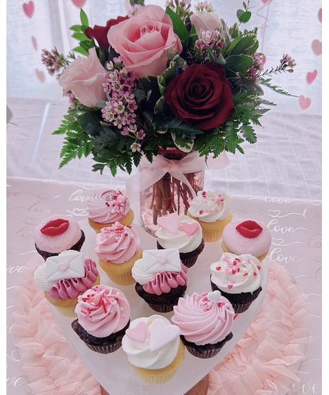 A Valentine’s Day gift set featuring a rose bouquet in pink, red, and blush tones in a keepsake vase with a ribbon, paired with a set of  Valentine-themed Blue Crab Cupcakes.