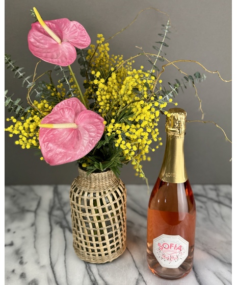 A spring floral arrangement featuring golden-yellow mimosa flowers, eucalyptus leaves, and willow branches in a natural rattan vase. Soft and rustic.