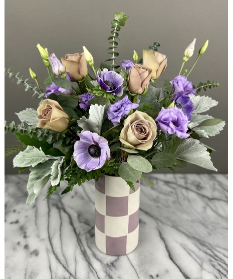 A floral arrangement of lavender-toned flowers displayed in a trendy checkered vase.