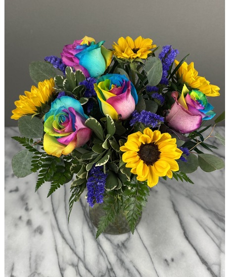 A floral arrangement featuring sunflowers and rainbow roses. The smaller size includes 3 sunflowers and 3 roses, while the larger size features 6 sunflowers and 6 roses. 