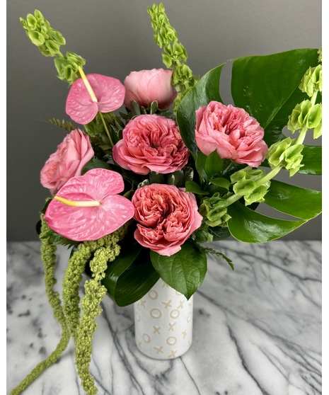 A designer's choice floral arrangement in a white ceramic vase with gold XOXO patterns. Features a mix of colorful seasonal blooms perfect for romantic occasions.