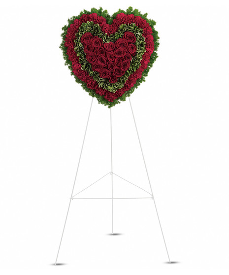 A heart-shaped sympathy wreath of rich red flowers with green accents, displayed on a standing easel, symbolizing eternal love and remembrance.